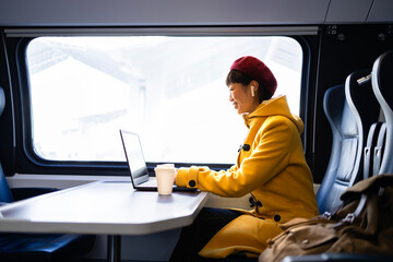 Female passenger working on laptop computer and enjoying comfortable train interior while commuting to work.