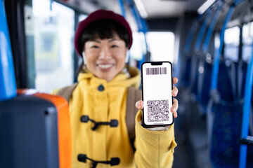 Smiling woman showing digital ticket on her phone while traveling by public bus transportation.