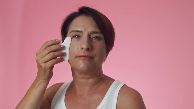 Medium close up of Gen X woman practicing anti-wrinkle massage using gua sha tool on face