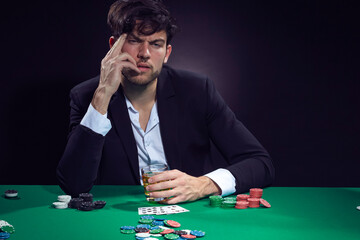 Addiction Ideas. Sad Depressed Handsome Caucasian Brunet Pocker Player At Pocker Table With Chips and Cards Drinking Alcohol.