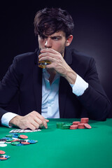 Addiction Ideas. Sad Depressed Handsome Caucasian Brunet Pocker Player At Pocker Table With Chips and Cards Drinking Alcohol