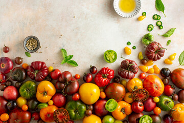 Ripe sweet tomatoes of different varieties and colors with herbs, pepper and olive oil on a beige background with a place for text. Top view.