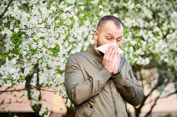 Man allergic suffering from seasonal allergy at spring in blossoming garden at springtime. Man...