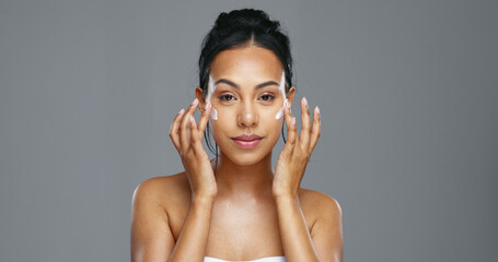 Fototapeta premium Face, skincare and happy woman apply cream in studio isolated on gray background mockup. Portrait, natural beauty and model with moisturizer, cosmetics and product for wellness, dermatology or health