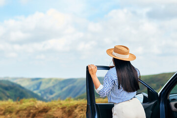 Back view of young beautiful woman traveling by car in the mountains, summer vacation and adventure