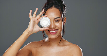 Happy woman, face and cream for skincare, beauty or cosmetics against a grey studio background....