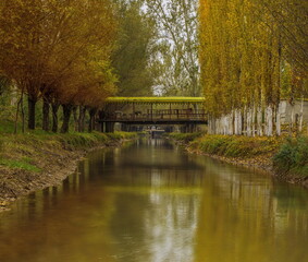 Fototapeta na wymiar A covered bridge over a picturesque canal lined with dense autumn trees on both sides