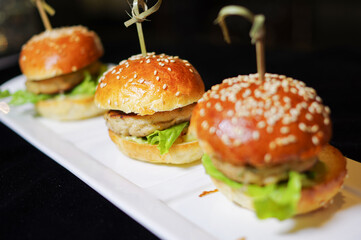 Sliders mini burgers on white plate with black background bar refreshment snack close up view