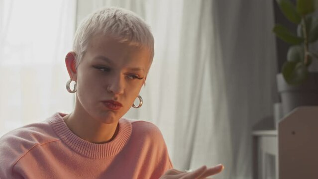 Young Caucasian woman with short blond hair using laptop while having conversation with female colleague with help of sign language