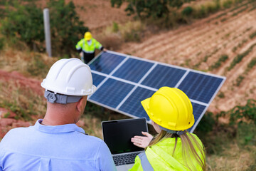 technician specialist and engineers examining solar panel using digital laptop computer in solar farm. solar panel cleaning officer background..