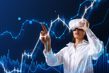 Attractive young european businesswoman with VR glasses using glowing and growing business chart on blurry blue background. Financial growth, virtual reality, trade and stock concept.
