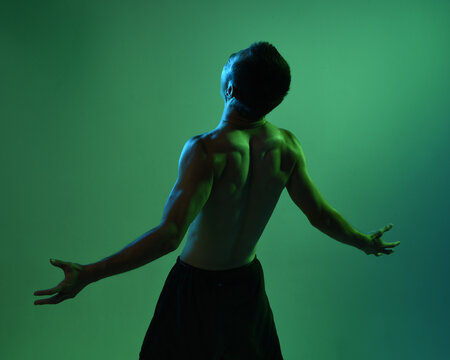 Close up portrait of fit asian male model, shirtless with muscles. gestural ti chi inspired posing with arms reaching out Isolated on a moody dark green studio background with silhouette.
