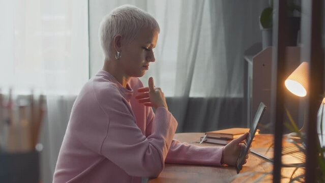 Waist up of young short-haired blond woman with hard of hearing video chatting on digital tablet using sign language while sitting by desk at home