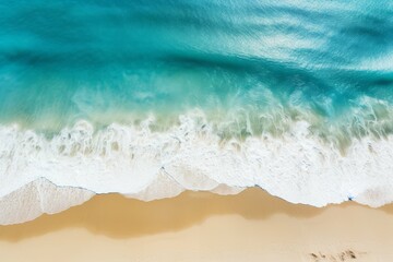 Fototapeta na wymiar Aerial shot of turquoise waves crashing onto a sandy beach shore.