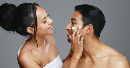 Couple, smile and love for skincare, happy and portrait with moisturizer in studio by gray...