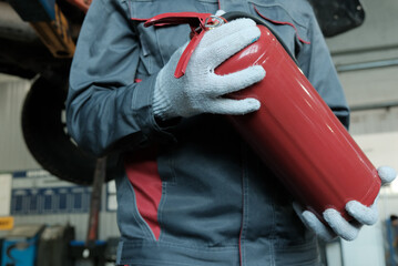 Fire safety in a car service station. An auto mechanic holds a fire extinguisher in his hands....