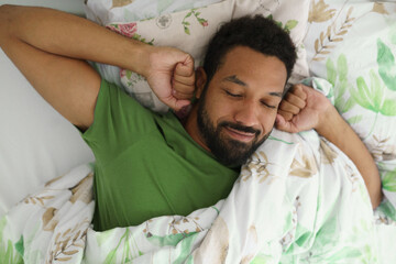 Top view of man waking up in bed, stretching arms, smiling in the morning.