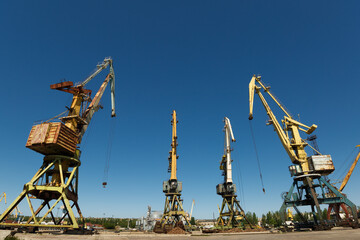 Decommissioned harbor cranes stand idle in disrepair at derelict seaport. Rusting machinery...