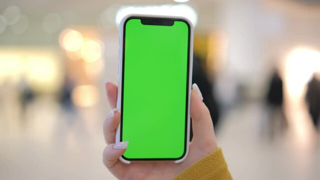 Use green screen for copy space closeup. Chroma key mock-up on smartphone in hand. Woman holds mobile phone and swipes photos or pictures in the mall 4K