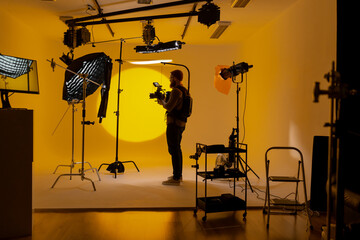 Videographer in film studio with vibrant yellow background