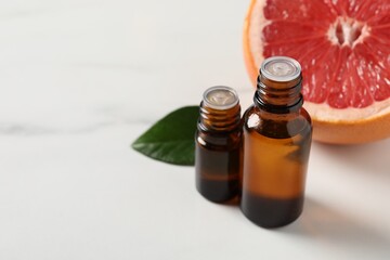 Grapefruit essential oil in bottles, leaf and fruit on white table, closeup. Space for text