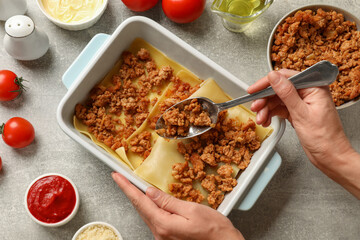 Woman making lasagna at light grey textured table, top view