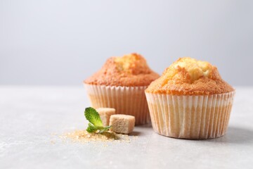 Delicious sweet muffins and brown sugar on light grey textured table, closeup. Space for text