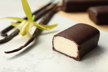 Glazed curd cheese bars, vanilla pods and flower on white table, closeup