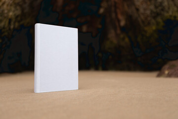 Book with a white cover without texts or drawings placed on the rocks of the coast