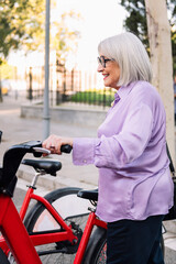 Fototapeta na wymiar smiling senior woman taking rental bike from parking row, concept of sustainable mobility and active lifestyle in elderly people