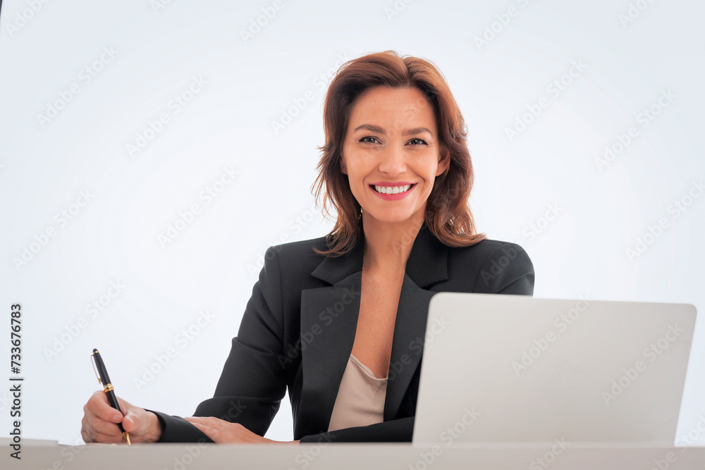 Wall mural Studio shot of an attractive mid aged woman sitting at desk and using laptop against isolated white background