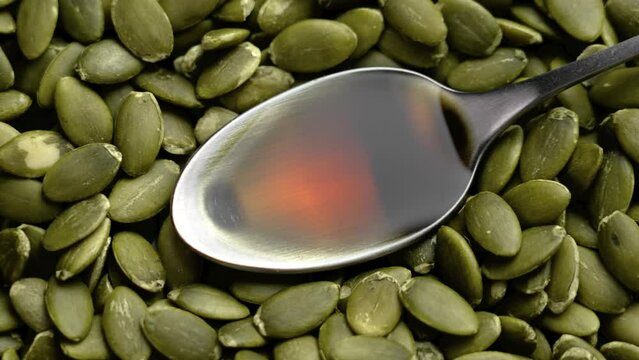 Pumpkin seed oil in metal spoon with pile of peeled kernels. Natural nutritious source of unsaturated fatty acids