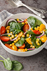 Summer salad of baby spinach, corn, cherry tomatoes and onions dressed with olive oil close-up in a bowl on the table. Vertical