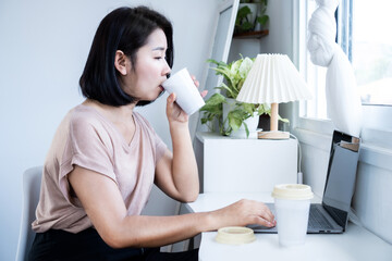 caffeine addiction concept with Asian woman drinking too much coffee while working on computer with cup of coffee on desk