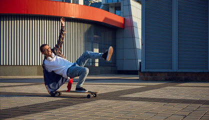 Excited skilled hipster guy making stunt on skateboard riding fast