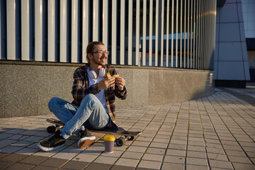 Hipster man wearing fashion trendy outfit with longboard eating sandwich