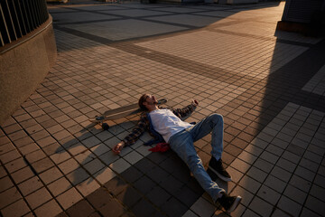 Tired hipster guy lying on skateboard after training relaxing in sunset