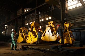 Industrial workers inspect yellow grapples in factory setting. Heavy equipment manufacturing...