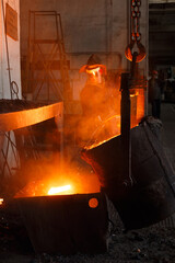 Worker in protective gear pours molten metal at steel mill. Industrial foundry scene showcasing...