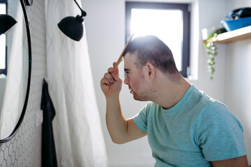 Young man with down syndrome in bathroom, combing his hairs.