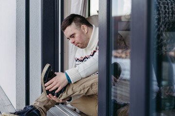 Portrait of young man with Down syndrome putting on shoes, sitting on floor.
