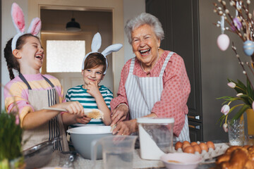 Grandmother with grandchildren preparing traditional easter meals, baking cakes and sweets. Passing down family recipes, custom and stories. - 733685581