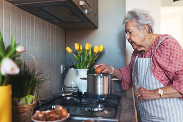 Senior woman preparing traditional easter meals for family, boiling eggs. Recreating family...