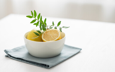 Fresh lemons in a bowl on a white wooden table in front of a window with morning natural light.
