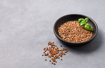 Raw buckwheat grains with fresh herbs in a wooden bowl on a light background.
