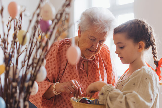 Grandmother with grandaughter decorating pussy willows branches, putting easter eggs on them.