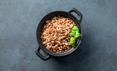 Buckwheat porridge with fresh herbs in a black pan on a dark  background.