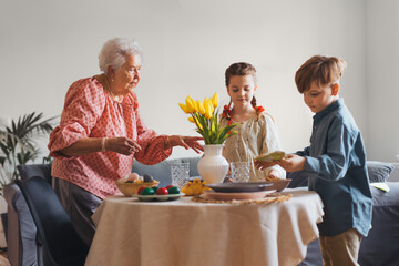 Grandmother with grandchildren setting table for traditional easter lunch. Recreating family traditions and customs.