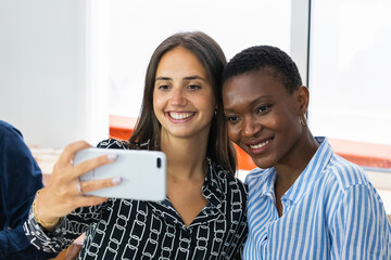 Smiling multiethnic coworkers taking selfie during break in office