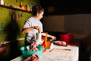 Woman mincing raw meat with meat grinder in kitchen
